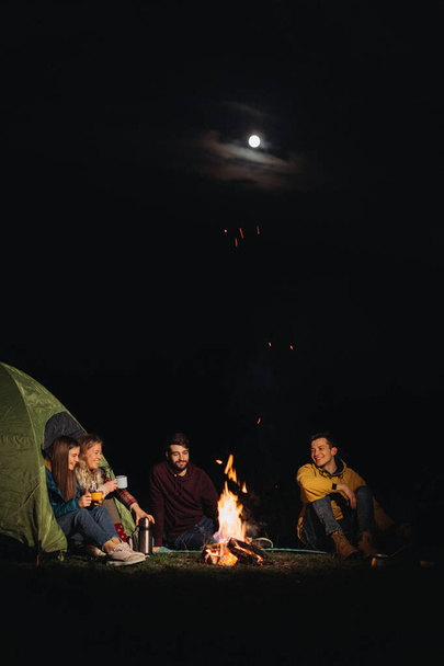 friends travelers sitting in front of bonfire at night  - Photo, Image