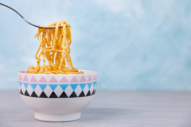 Noodles with sauce in colored bowl with fork, appetite spaghetti on a blue background. - Fotó, kép