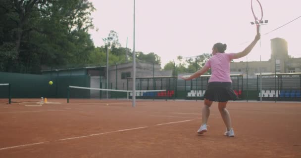  Joven mujer caucásica jugando al tenis en una cancha, devolviendo una pelota en cámara lenta - Metraje, vídeo