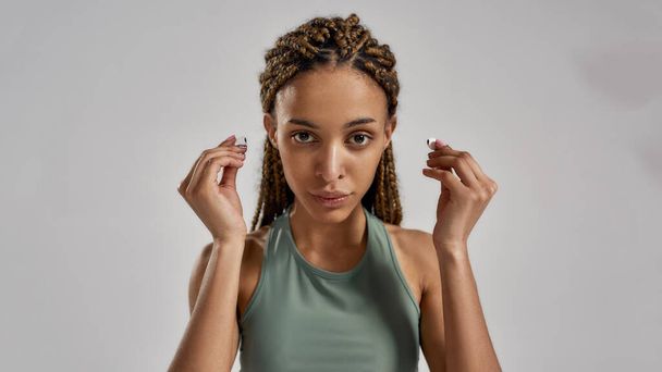 Listening to music during a workout. Young sporty african sporty woman wearing wireless earbuds and looking at camera while standing isolated over grey background - Fotó, kép