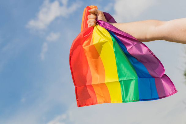 el hombre sostiene la bandera del arco iris del movimiento LGBT fuertemente apretada en su mano. Una expresión de fuerza y determinación en la lucha por la igualdad - Foto, Imagen