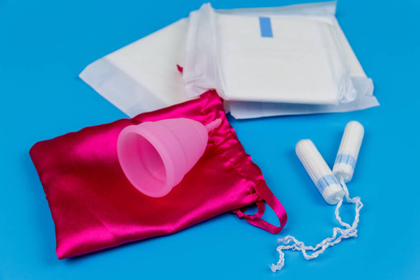 Hygienická podložka, tampóny a menstruační kelímek na modrém pozadí. Koncepce kritických dnů, menstruace, ženská hygiena - Fotografie, Obrázek