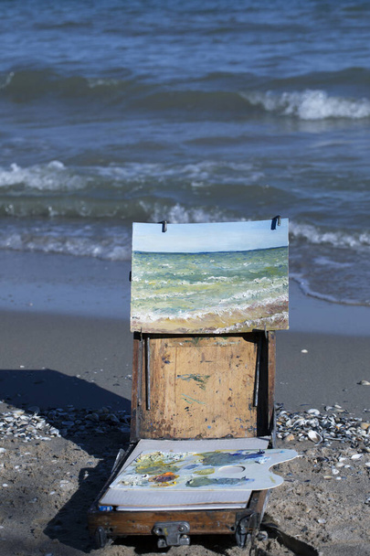 Skizze eines Tagesmeeres mit Wellen in Ölfarben auf Leinwand gemalt, auf Staffelei vor dem Hintergrund des Meeres, vertikales Format - Foto, Bild