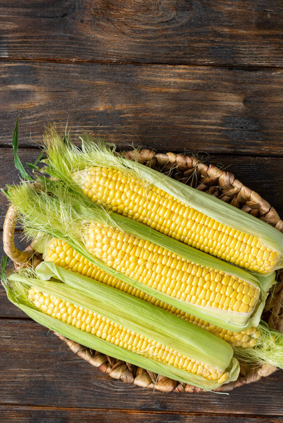 Corn. Fresh raw corn in a basket on a brown wooden table. The concept of the fall harvest. Top view with space for text - Photo, Image