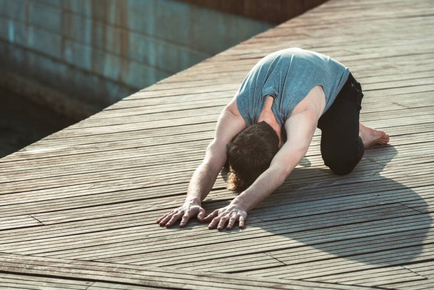 Balasana es una postura de yoga para evitar el dolor de espalda, un joven la practica. - Foto, Imagen