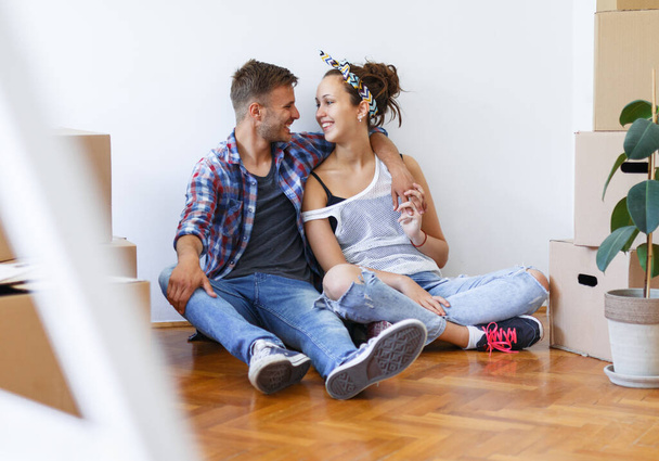 Moving in to a new home. Young couple in love sitting on the floor surrounded by boxes - Photo, Image