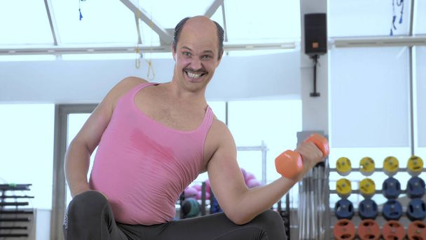 medium shot. Bald funny man is training with dumbbells in the gym - Foto, afbeelding