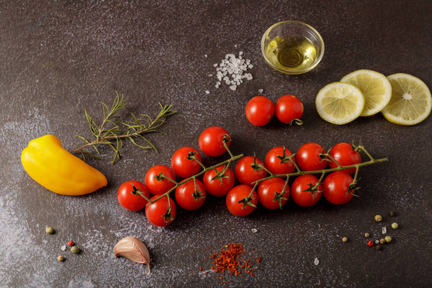 Verse rode kerstomaten, rozemarijn, olie, schijfje citroen en specerijen op een stenen bord. Kaart met kopieerruimte - Foto, afbeelding