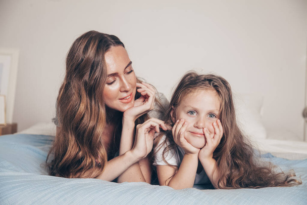 Close up portrait of happy loving family lying relaxing enjoying in bedroom together. Mother and her cute preschool daughter child girl in pajamas playing and hugging in bed. Happy mother's day - Zdjęcie, obraz