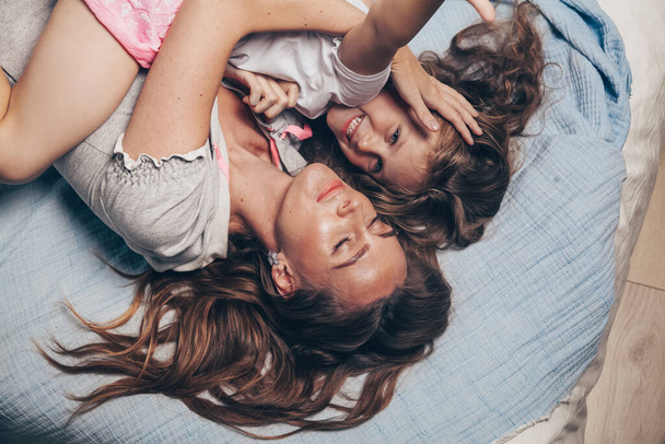 Happy loving family lying relaxing enjoying in bedroom together. Mother and her cute preschool daughter child girl in pajamas playing and hugging in bed in the morning top view. Happy mother's day - Foto, Bild