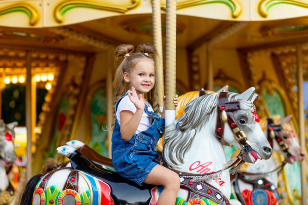 joyeuse petite fille monte un carrousel sur un cheval dans un parc d'attractions en été - Photo, image