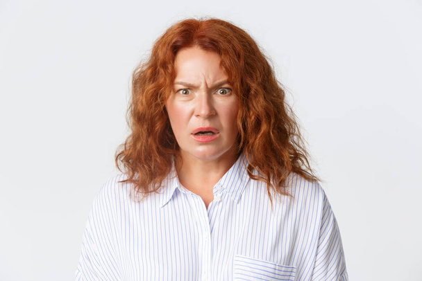 People, emotions and lifestyle concept. Close-up of frustrated and displeased middle-aged woman cringe from something disgusting and confusing, standing white background - Foto, imagen