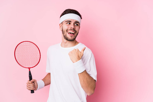 Young caucasian man playing badminton isolated points with thumb finger away, laughing and carefree. - Photo, Image