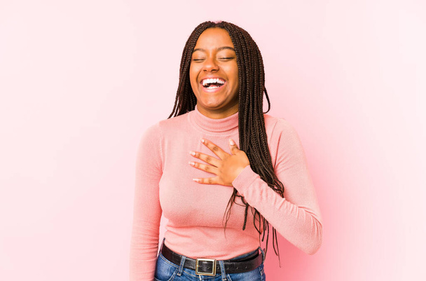 Młoda Afroamerykanka odizolowana na różowym tle śmieje się głośno trzymając rękę na piersi. - Zdjęcie, obraz