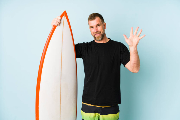 Surfen człowiek odizolowany na niebieskim tle uśmiechnięty radosny pokazując numer pięć z palcami. - Zdjęcie, obraz