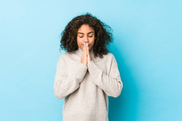 Młoda Afroamerykanka kręcone włosy kobieta trzymając się za ręce w modlitwie blisko ust, czuje się pewnie. - Zdjęcie, obraz