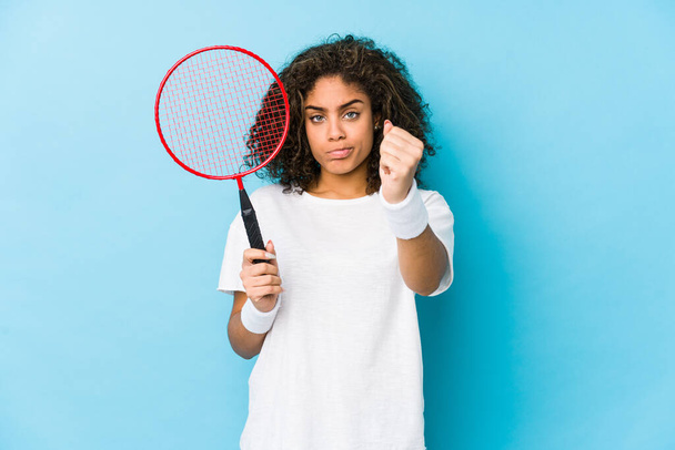 Junge Afroamerikanerin spielt Badminton und zeigt der Kamera die Faust, aggressiver Gesichtsausdruck. - Foto, Bild