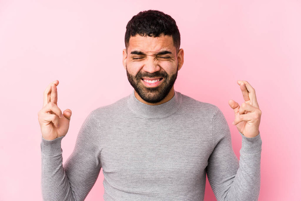 Young latin man against a pink background isolated crossing fingers for having luck - Foto, Imagen