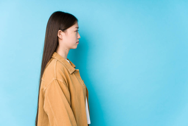 Jonge Chinese vrouw poseren in een blauwe achtergrond geïsoleerde staren links, zijwaarts poseren. - Foto, afbeelding