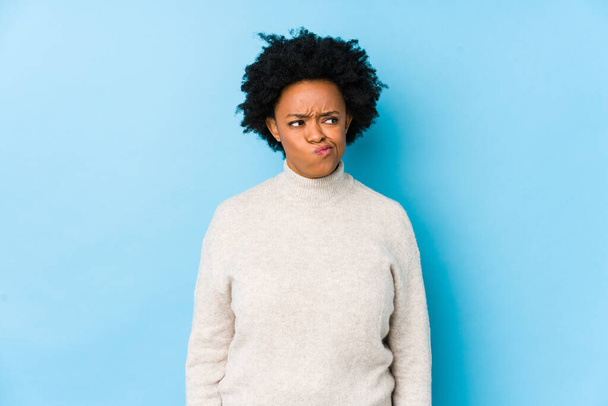 Afroameričanka středního věku na modrém pozadí izolovaná zmatená, nejistá a nejistá. - Fotografie, Obrázek