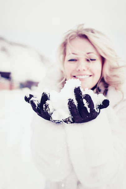 Beautiful blond woman in white fur coat enjoying fresh snow in her hands. - Foto, Bild