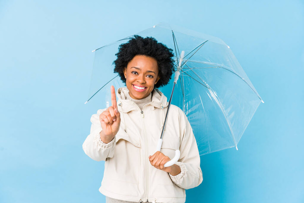 Mladý africký Američan žena drží deštník izolovaný ukazující číslo jedna s prstem. - Fotografie, Obrázek