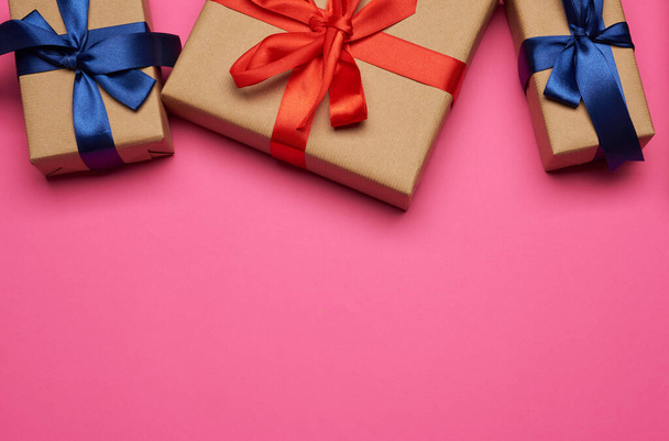 ajándékdobozok barna papírba csomagolva, piros és kék masnival megkötözve, ajándékok rózsaszín alapon, szöveges hely - Fotó, kép