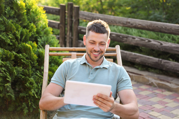 Happy man using tablet in deck chair outdoors - Foto, imagen