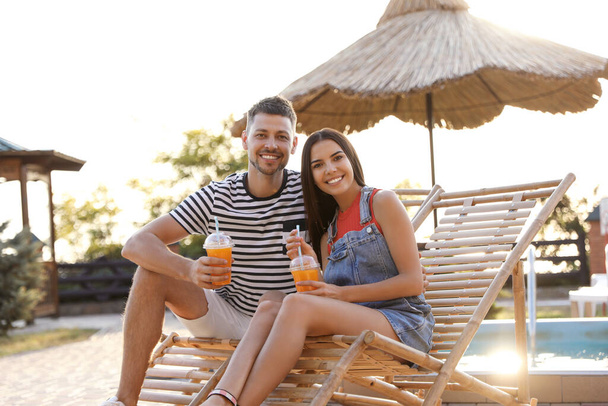 Happy couple with cups of refreshing drink resting in deck chairs outdoors - Foto, afbeelding