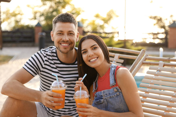 Happy couple with cups of refreshing drink resting in deck chairs outdoors - Photo, Image