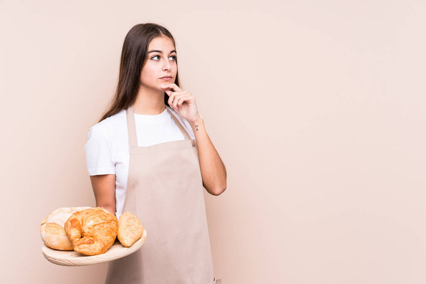 Junge kaukasische Bäckerin schaut mit zweifelndem und skeptischem Gesichtsausdruck zur Seite. - Foto, Bild