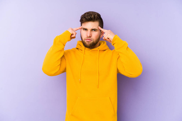 Young man isolated on purple background focused on a task, keeping forefingers pointing head. - Photo, Image