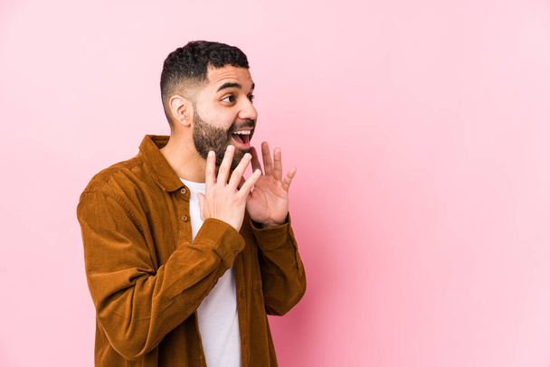 Jonge latijn man tegen een roze achtergrond geïsoleerde schreeuwt luid, houdt ogen geopend en handen gespannen. - Foto, afbeelding