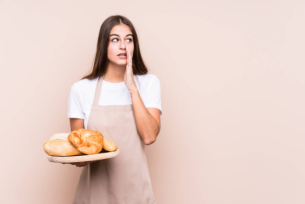 Young caucasian baker woman isolated is saying a secret hot braking news and looking aside - Fotografie, Obrázek