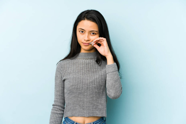 Young chinese woman isolated on a blue background with fingers on lips keeping a secret. - Foto, immagini