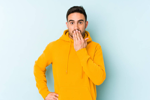 Young caucasian man isolated on blue background shocked, covering mouth with hands, anxious to discover something new. - Foto, Bild