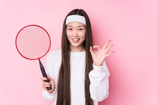 młody chiński kobieta gra badminton odizolowany wesoły i pewny siebie pokazując ok gest. - Zdjęcie, obraz