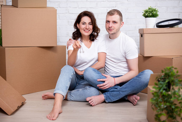 día de mudanza - feliz pareja joven mostrando las llaves de su nueva casa o piso rodeado de cajas de cartón - Foto, Imagen