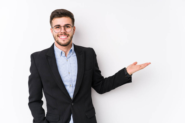 Jonge blanke zakenman poseert in een witte achtergrond geïsoleerd Jonge Kaukasische zakenman toont een kopieerruimte op een handpalm en houdt een andere hand op de taille. - Foto, afbeelding