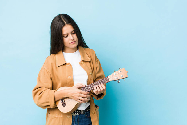 Young caucasian woman playing ukelele isolated on a blue background - Фото, зображення