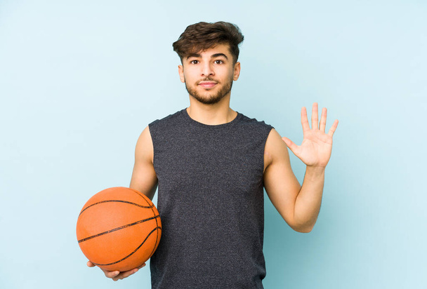 Young arabian man playing basket isolated smiling cheerful showing number five with fingers. - Photo, Image