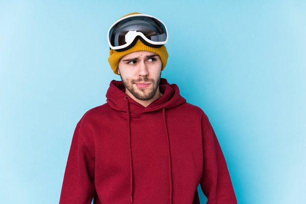 Jeune homme caucasien portant un vêtement de ski isolé confus, se sent douteux et incertain. - Photo, image