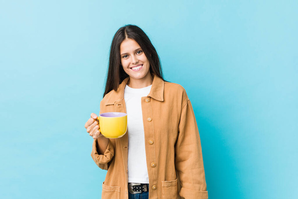 Νεαρή λευκή γυναίκα που κρατάει μια κούπα καφέ χαρούμενη, χαμογελαστή και χαρούμενη. - Φωτογραφία, εικόνα