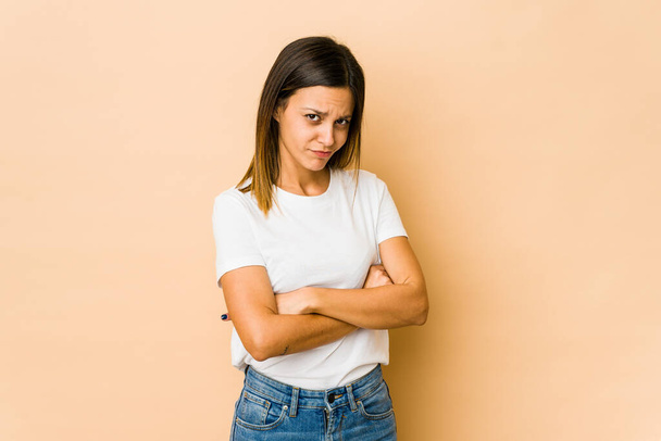Young woman isolated on beige background frowning face in displeasure, keeps arms folded. - Photo, Image