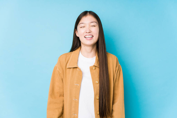Mulher chinesa jovem posando em um fundo azul isolado ri e fecha os olhos, se sente relaxado e feliz. - Foto, Imagem