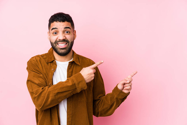 Giovane uomo latino su uno sfondo rosa isolato scioccato indicando con le dita indice uno spazio di copia. - Foto, immagini