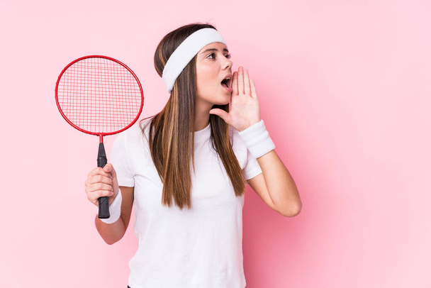 Young caucasian woman playing badminton isolated shouting and holding palm near opened mouth. - Photo, Image