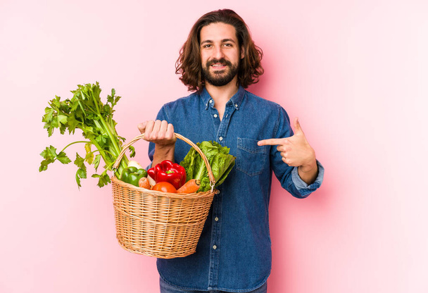 Junger Mann pflückt Bio-Gemüse aus seinem Garten und zeigt mit der Hand auf ein T-Shirt, stolz und selbstbewusst - Foto, Bild