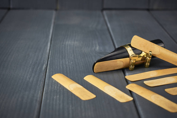 σαξόφωνο επιστόμιο και καλάμι με σφιγκτήρα και χρυσό υλικό μαζί με ανταλλακτικές καλάμια σε γκρι ξύλινο φόντο - Φωτογραφία, εικόνα