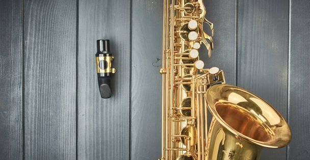 Саксофонный мундштук, разобранный с корпуса инструмента, с зубной палкой и золотым зажимом, на серой древесине - Фото, изображение